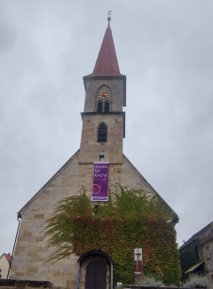 Foto der St. Bartholomäuskirche mit Wein und Plakat zur Kirchenvorstandswahl 2024